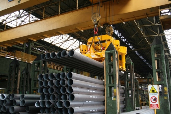 Palonnier électromagnétique en cours de levage de tubes dans un atelier sidérurgique.